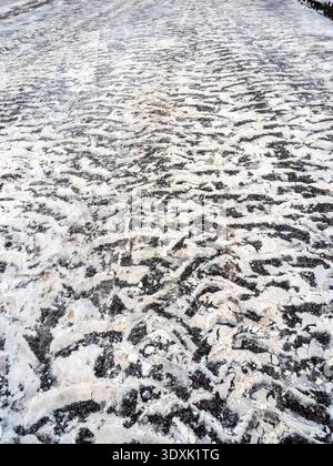 surface of asphalt road with snow car tires imprint in city on cloudy winter day Stock Photo