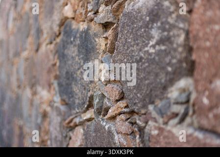 Close-up of a rustic stone wall with roughly hewn stones in reddish-brown tones. Angled view. Stock Photo