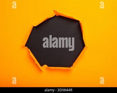 A bright orange paper with a torn hole that reveals a textured black background. Stock Photo
