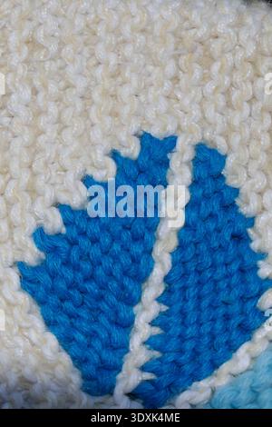 Macro view of a blue leaf motif knitted into white wool fabric, highlighting detailed yarn texture, handmade craftsmanship and decorative textile desi Stock Photo