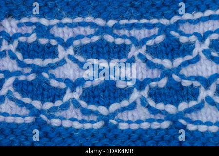 Detailed macro view of a blue and white repeating knitted pattern, showcasing wool yarn texture, craftsmanship and decorative textile design in handma Stock Photo