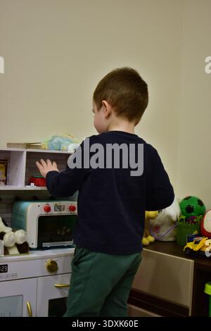 Toddler boy playing with toy kitchen set at home, pretending to cook. Indoor lifestyle scene with educational toys, imagination development and creati Stock Photo