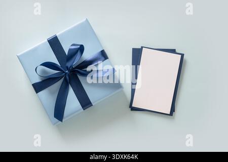 Blue wrapped present with blank greeting card on pastel background. Fathers Day concept. Minimal layout. Stock Photo