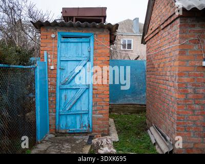 detached old brick outhouse with blue painted wooden door in backyard of rustic house Stock Photo
