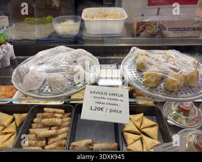 Steamed shrimp dumplings and samosas under plastic wrap in a display case at an Asian takeaway counter, with a price sign in French. Stock Photo