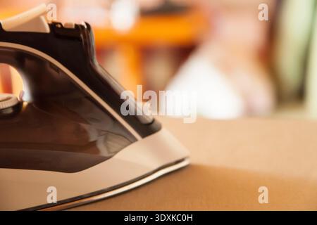 An iron on an ironing board with blurred household objects in the background Stock Photo