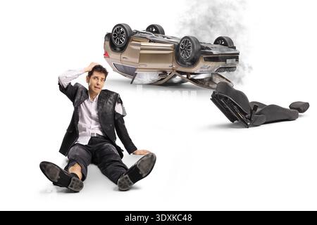 Shocked businessman in a torn suit sitting on the floor after a car accident and holding his head Stock Photo