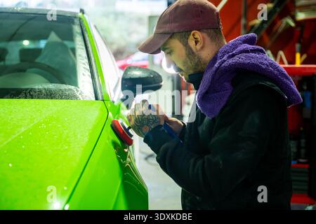Car mechanic polishing bright green vehicle paint in workshop Stock Photo