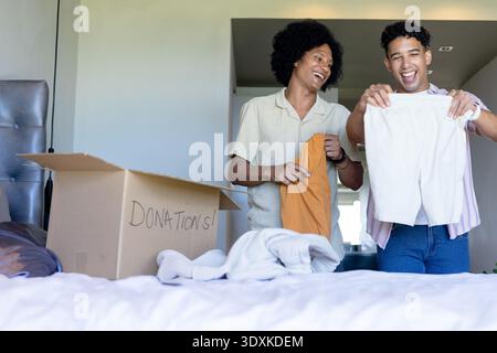 Two African American men standing by bed sorting clothing into cardboard box labeled DONATIONS Stock Photo