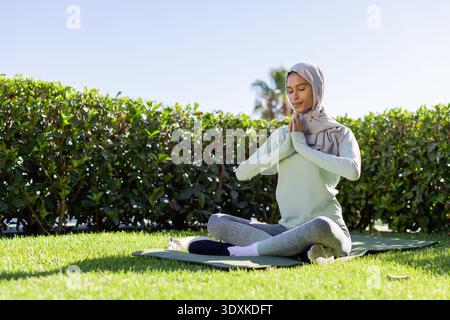 African American woman meditating on green yoga mat in garden in headscarf white shoes, copy space Stock Photo