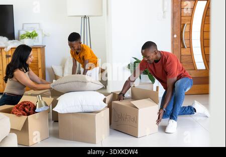 Diverse family packing cardboard boxes in living room near front door with donation box Stock Photo