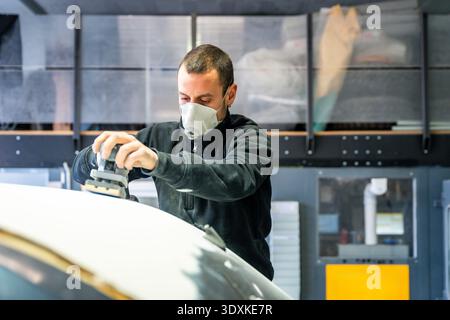 Mechanic sanding car body surface in repair shop Stock Photo