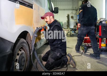Auto body mechanic sanding van surface in workshop Stock Photo