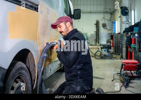 Mechanic sanding van body preparing for paint in repair shop Stock Photo