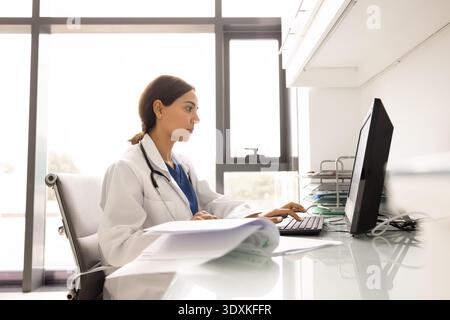 Focused female doctor in white coat working on desktop computer Stock Photo
