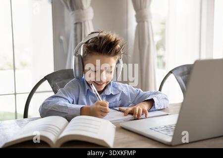 Smiling school boy studying remotely sit at table with laptop Stock Photo