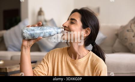 Close-up of smiling Latina woman drinking water from reusable bottle Stock Photo