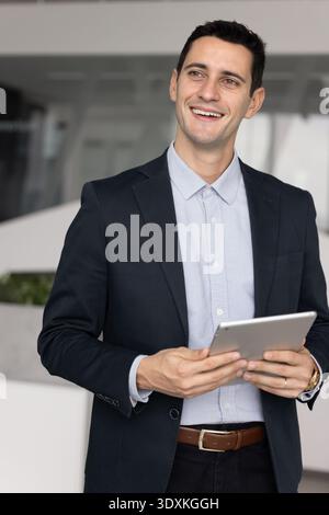 Smiling Hispanic businessman holding tablet looking away enjoying digital productivity Stock Photo