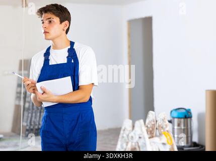 Portrait of man builder in construction overalls with documents in hands checks quality of completed repairs in apartment Stock Photo