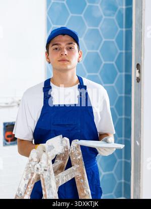 Construction worker in work clothes engaged in wall tiling work during overhauls indoors Stock Photo