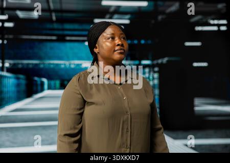 System administrator walking in data center with rigs supporting business needs. Woman in server hub doing checkup, ensuring infrastructure works at optimum performance for smooth operations Stock Photo