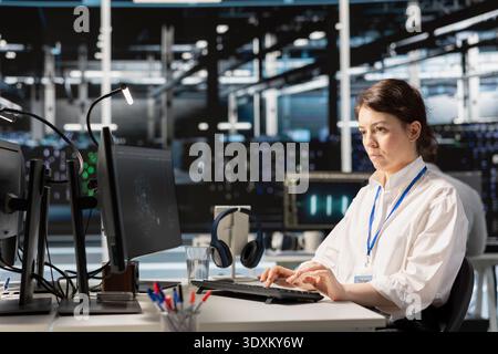 Woman in data center running diagnostic scripts on computer, examining equipment. Server room IT professional using PC to evaluate rackmounts performance metrics, maintaining system stability Stock Photo