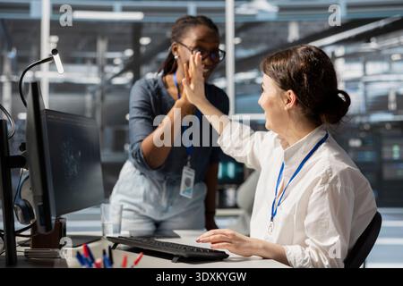 Pleased server farm manager does high five with employee after completing operations. Cheerful supervisor praising technician accomplishments in data center after checking performance report Stock Photo
