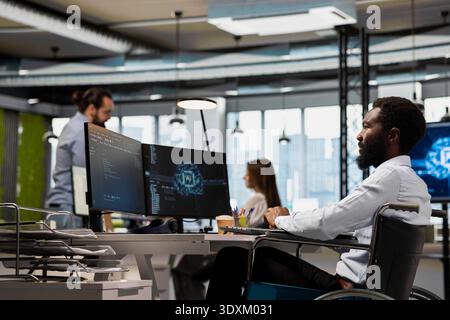 System administrator with paraplegia in office automating repetitive tasks with AI scripts. IT specialist in wheelchair using artificial intelligence to speed up feature implementation Stock Photo