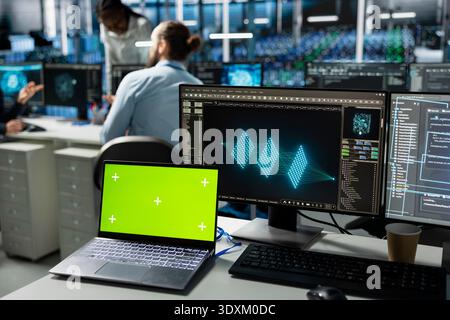 Green screen mockup laptop used by engineers in data center installing upgraded server systems with AI. Chroma key notebook in server hub with workers upgrading gear using artificial intelligence Stock Photo