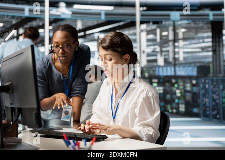Server farm teamworking colleagues using computer to analyze facility data patterns. Data center experts working together, using programming language algorithms on PC to analyze datasets Stock Photo