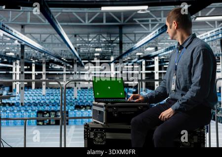 Data center employee using green screen notebook, minimizing downtime through predictive maintenance. Engineer using mockup laptop in server hub, implementing sustainable energy efficient technologies Stock Photo