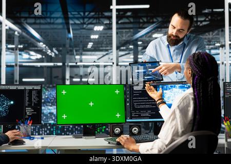 Coworkers coding in data center using green screen mockup PC, updating AI automation scripts. Server room colleagues using chroma key mockup computer, programming artificial intelligence algorithms Stock Photo