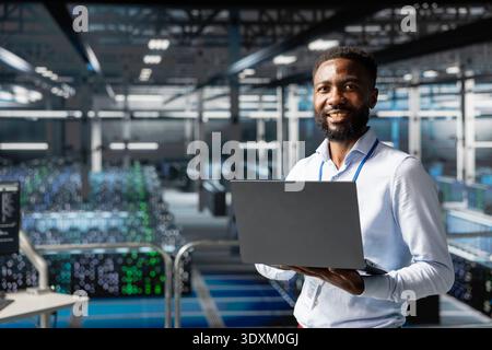 Portrait of confident engineer in server room reviews AI visualization on industrial platform, monitoring deep learning software development. Young man maintaining operational reliability. Stock Photo