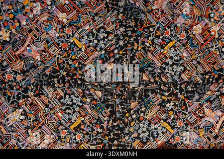 Sevilla, Spain - 23 Dec 23: Close-up of embroidered textile with small figures, houses and floral motifs on dark fabric, displayed at Casa Fabiola mus Stock Photo