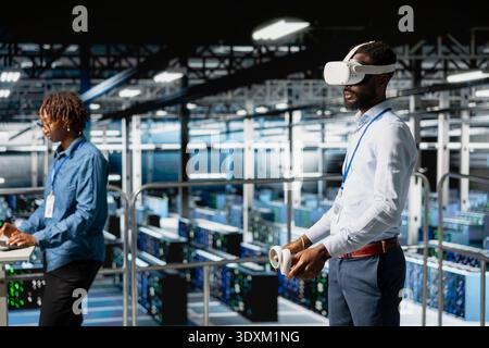 African american technician uses VR headset on industrial platform, using high tech tools to manage deep learning configuration for automation. LLM visualization in a server hub. Stock Photo
