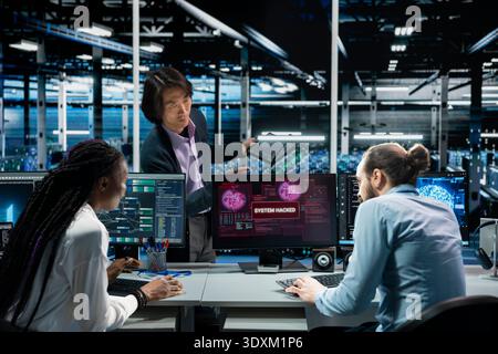 Computer scientists in AI server room cooperating to fix hacking incident involving theft of sensitive data. Data center colleagues trying to stop malware breaching security systems Stock Photo