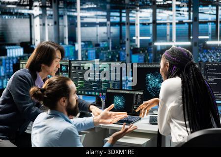 Multiethnic coworkers in server room using devices to review infrastructure diagnostics. Multiracial team in diverse data center analyzing performance data to maintain system uptime Stock Photo