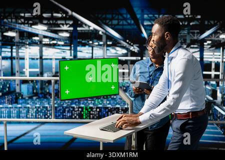 Data center engineers on industrial platform using isolated screen on pc, collaborating on software development tasks. Coworkers visualizing cloud computing engineering in server hub. Stock Photo