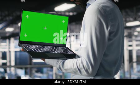 Technicians on data center industrial platform analyzing performance outputs on green screen laptop. Server hub engineering team finetuning server rig configurations using mockup notebook Stock Photo
