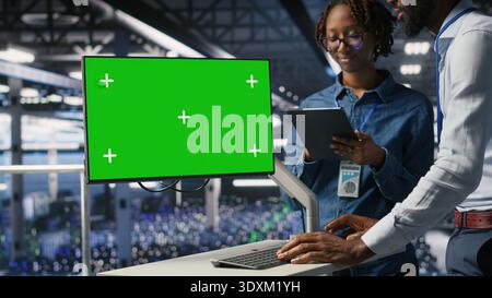 Server room coworkers doing brainstorming, using chroma key device to review diagnostics. Employees doing maintenance tasks in data center, looking at isolated screen monitor Stock Photo