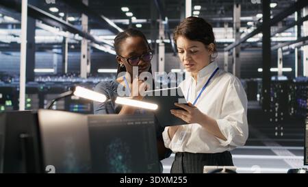 Teamworking engineers in data center integrate AI automation tools together during maintenance session. Server room colleagues configure machine learning models across server infrastructure, camera A Stock Photo