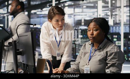 Data center team leader and IT expert reviewing performance dashboards of AI equipment rigs. Server room manager oversee system administrator examining machine learning algorithms on screen, camera A Stock Photo