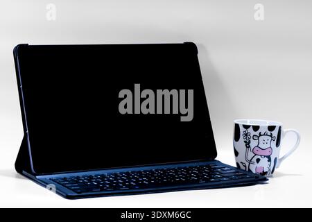 Modern tablet with detachable keyboard and blank screen beside coffee mug isolated on white background. Workspace mockup with copy space for website, Stock Photo