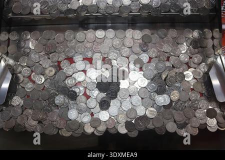 Dozens of coins appear suspended over the cash drop of a vintage arcade coin pusher or penny waterfall gaming machine. Stock Photo
