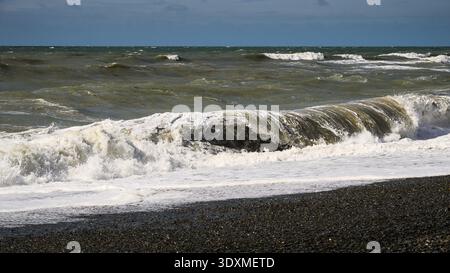 Angry storm waves roll ashore on stone beach creating surf Stock Photo