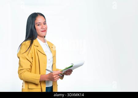 A professional Indonesian woman in a yellow blazer smiling while holding a clipboard and pen, perfect for office, management, and career themes. Stock Photo