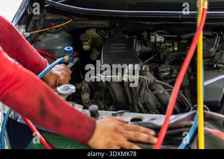 Mechanic checking car air conditioning system with manifold gauge set under open hood during vehicle maintenance repair in auto service garage close u Stock Photo