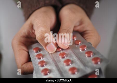 Hands hold a blister pack of red pills in a simple setting Stock Photo