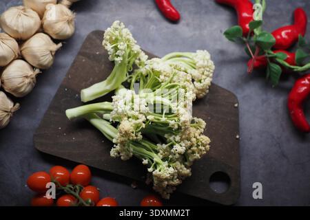 Broccoli and tomatoes are arranged with garlic and peppers on a board Stock Photo