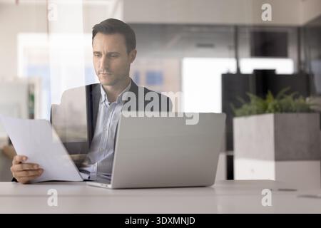 Focused Hispanic corporate professional reading paper contracts at office workplace Stock Photo